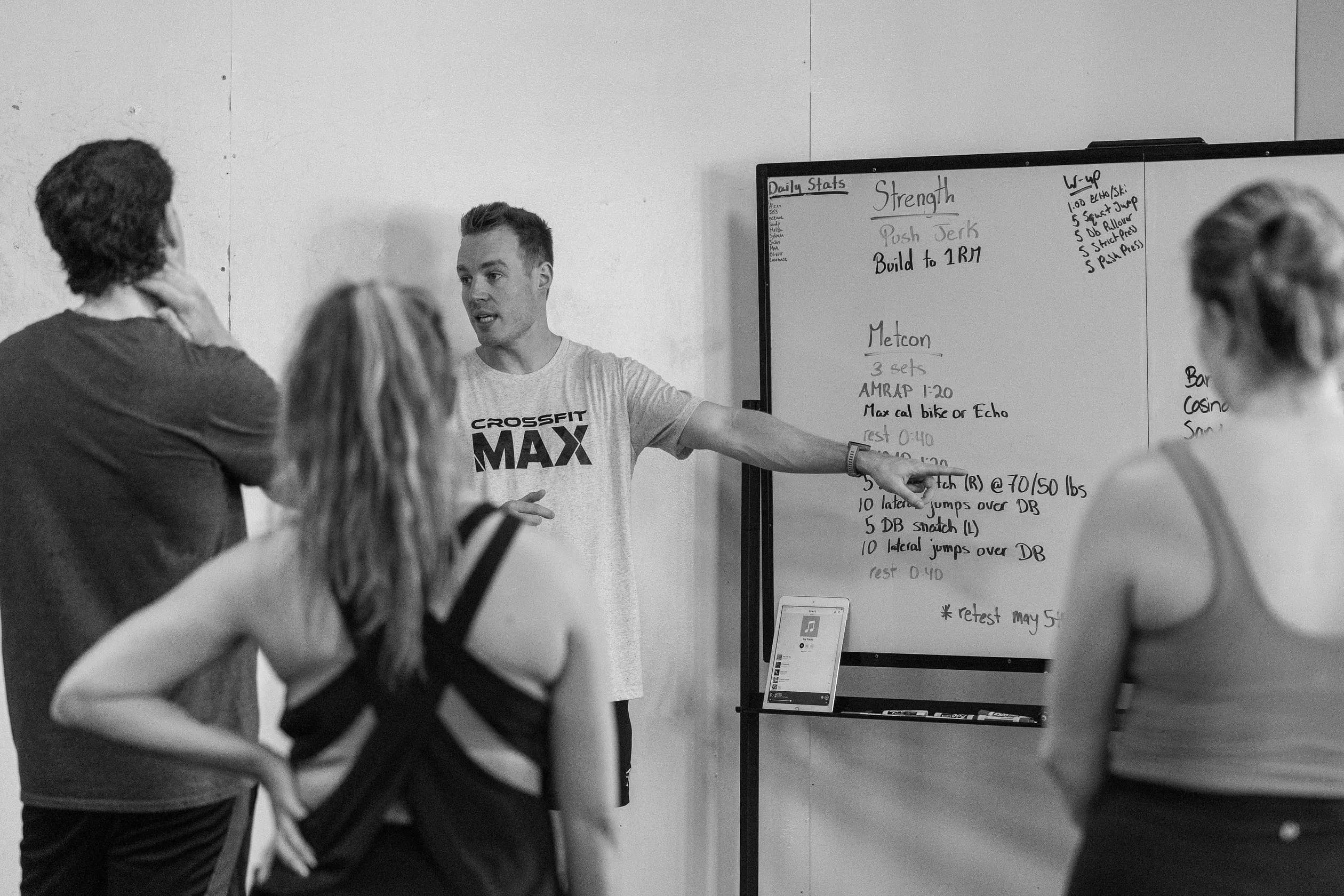A coach explains the day's workout at the whiteboard.
