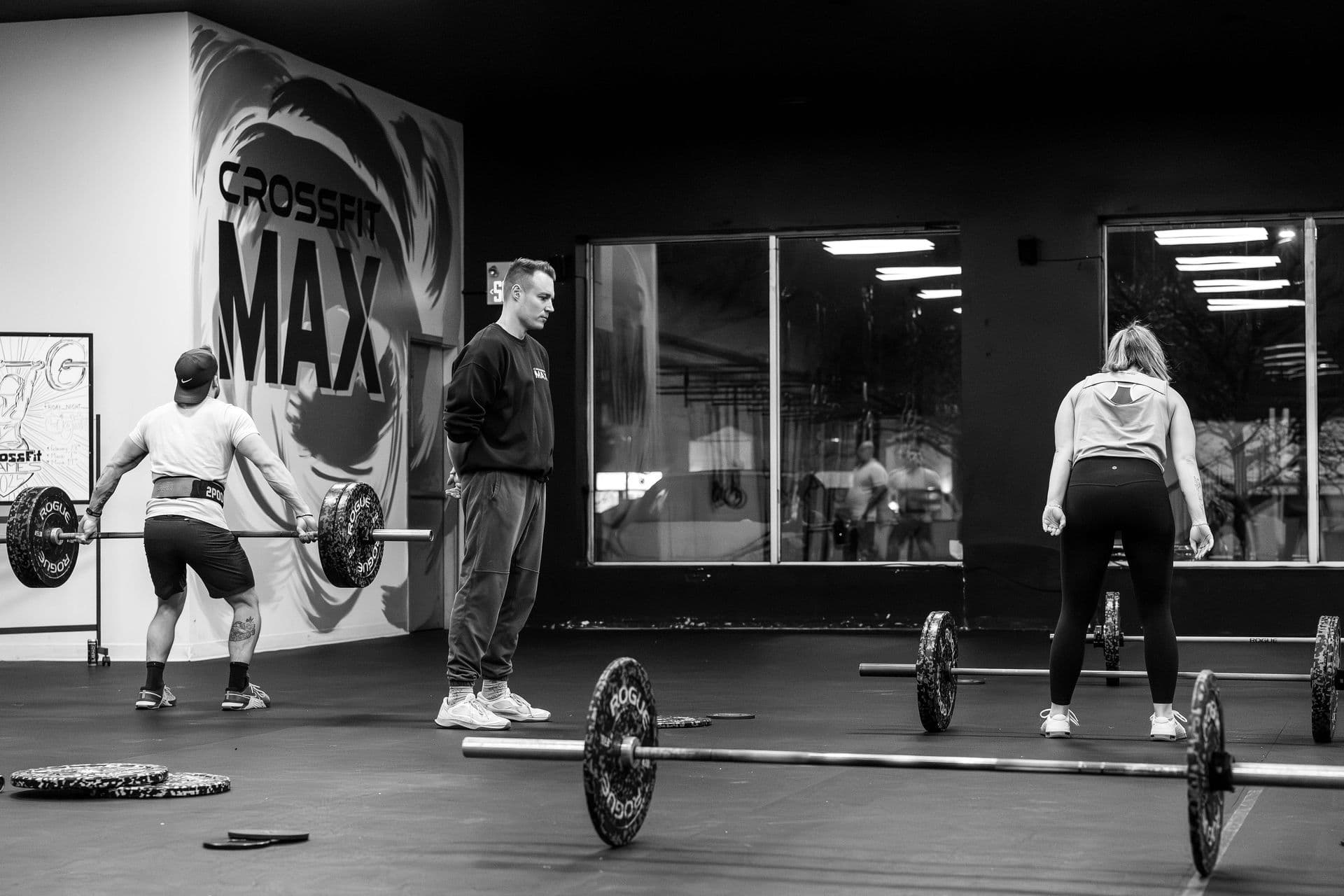 A coach watching two members deadlift beside the CrossFit Max mural.